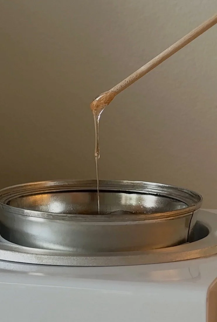 Close-up of a wooden stick dipping into a hot wax pot to showcase eyebrow waxing services.
