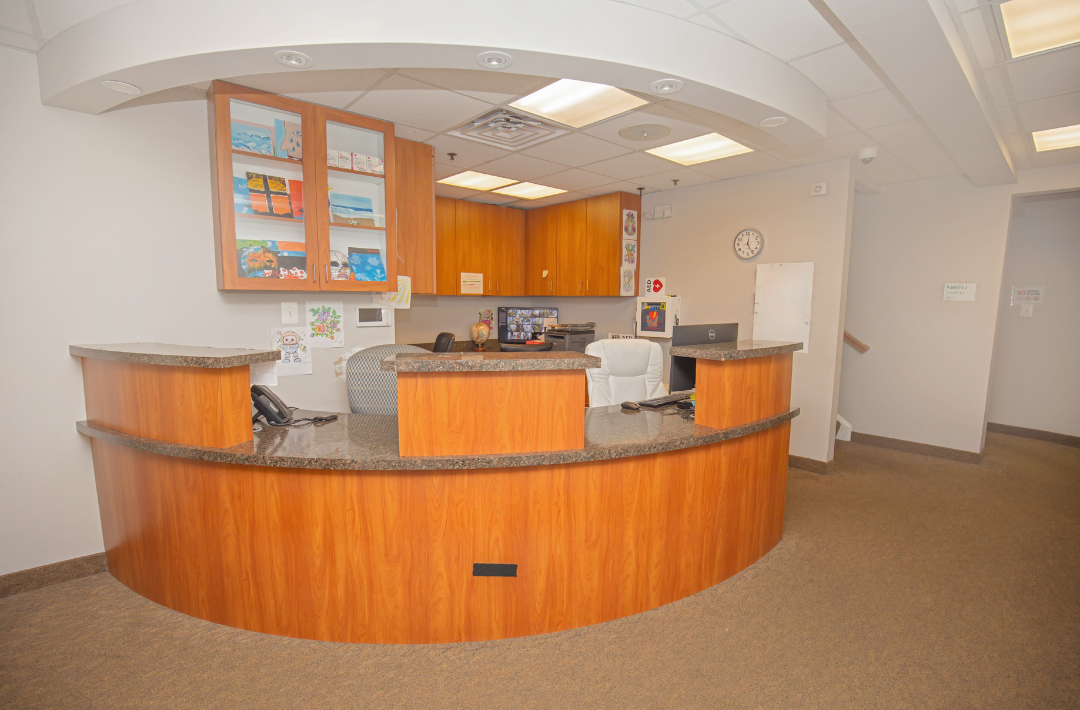 Front desk reception area made of wood with a granite countertop, equipped with phones and computers, in an office or clinic setting.