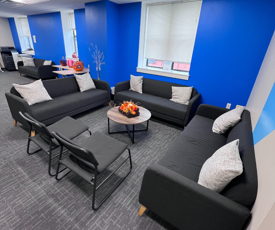 Waiting area with three chairs, a tufted sofa, a doorway with glass doors, and large windows with blinds in a healthcare or office building.