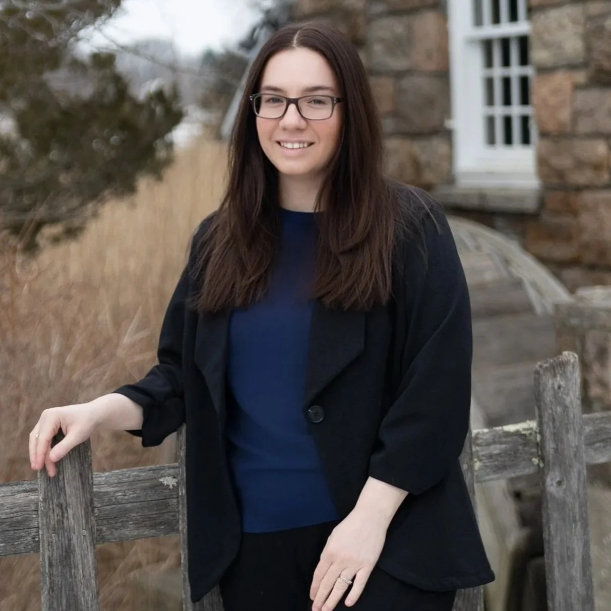 Portrait of a woman with blonde hair, wearing a white shirt and hoop earrings, smiling against a blurred beige background.