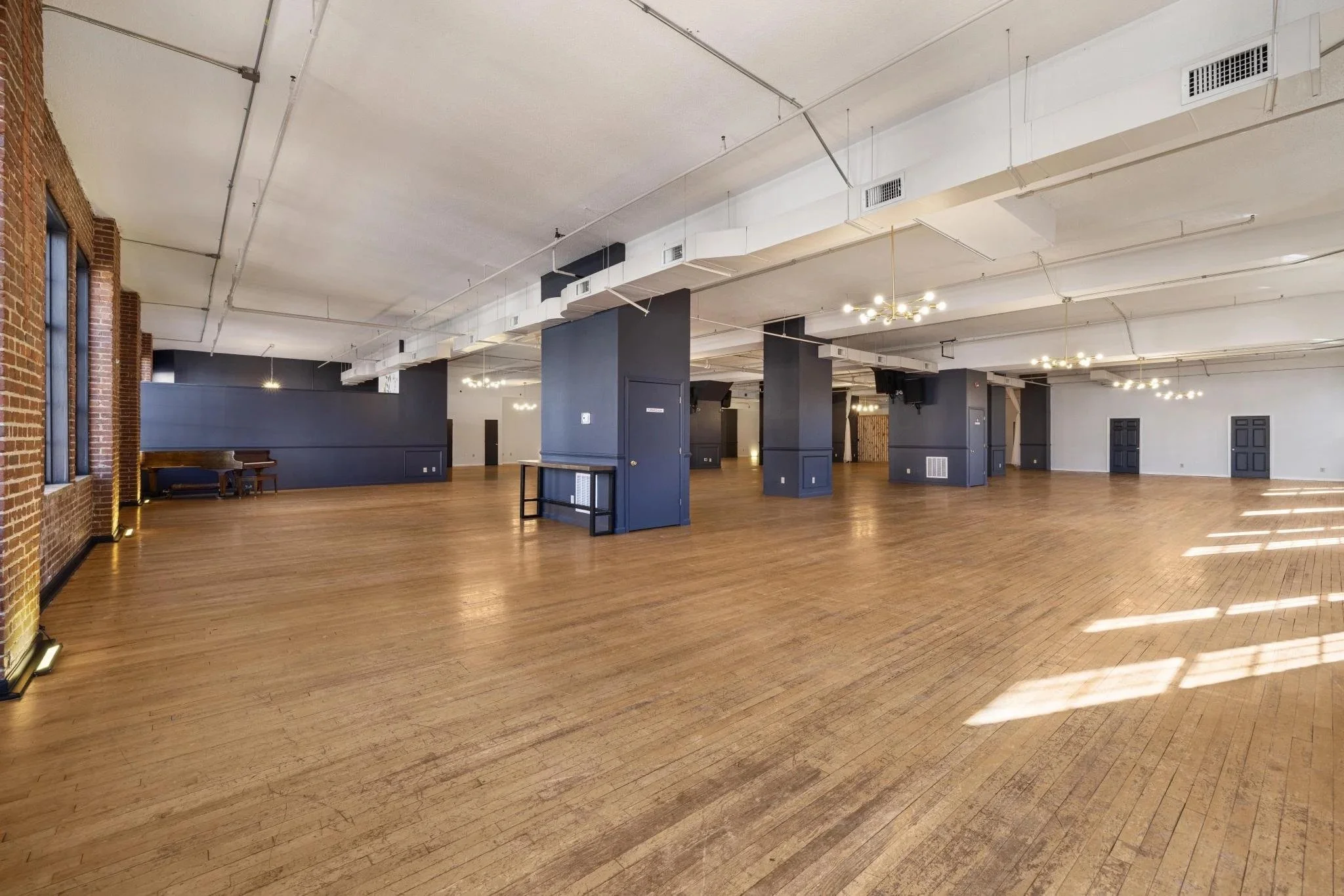 Wide-angle view of Monarch on Main’s main event room with navy columns, exposed brick, and elegant lighting fixtures.
