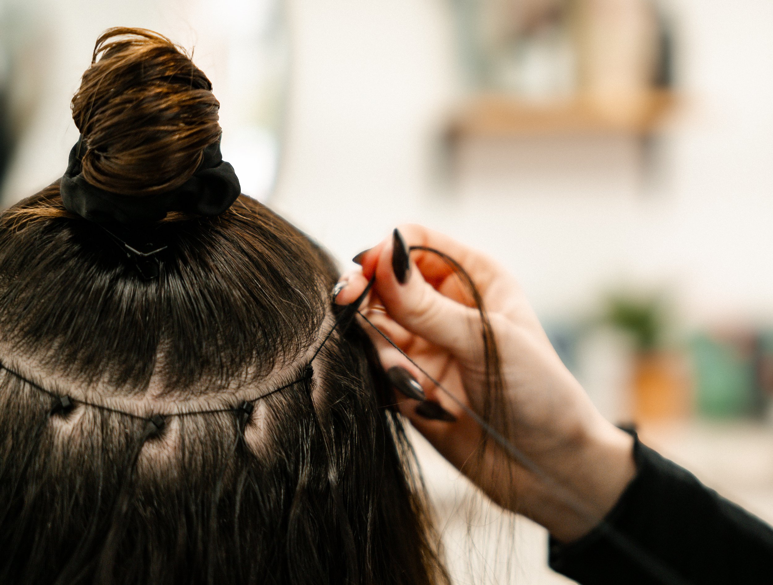 A person with dark hair is getting a hair treatment with a headband and hair clips, while another person is applying eyelash extensions or eyeliner with a tool.