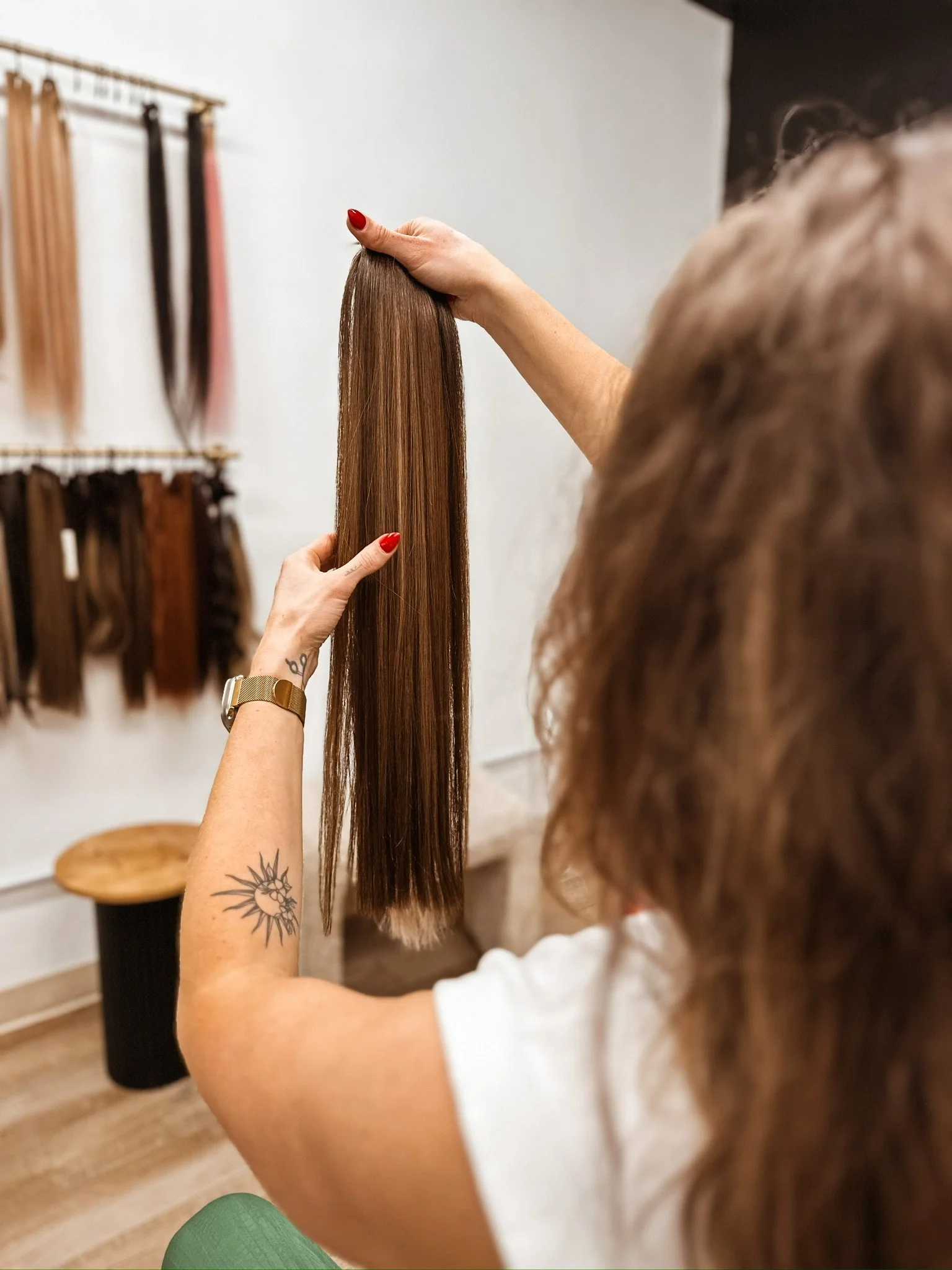 A person with a tattoo on their arm holding a section of long, straight, brown hair in a hair salon.