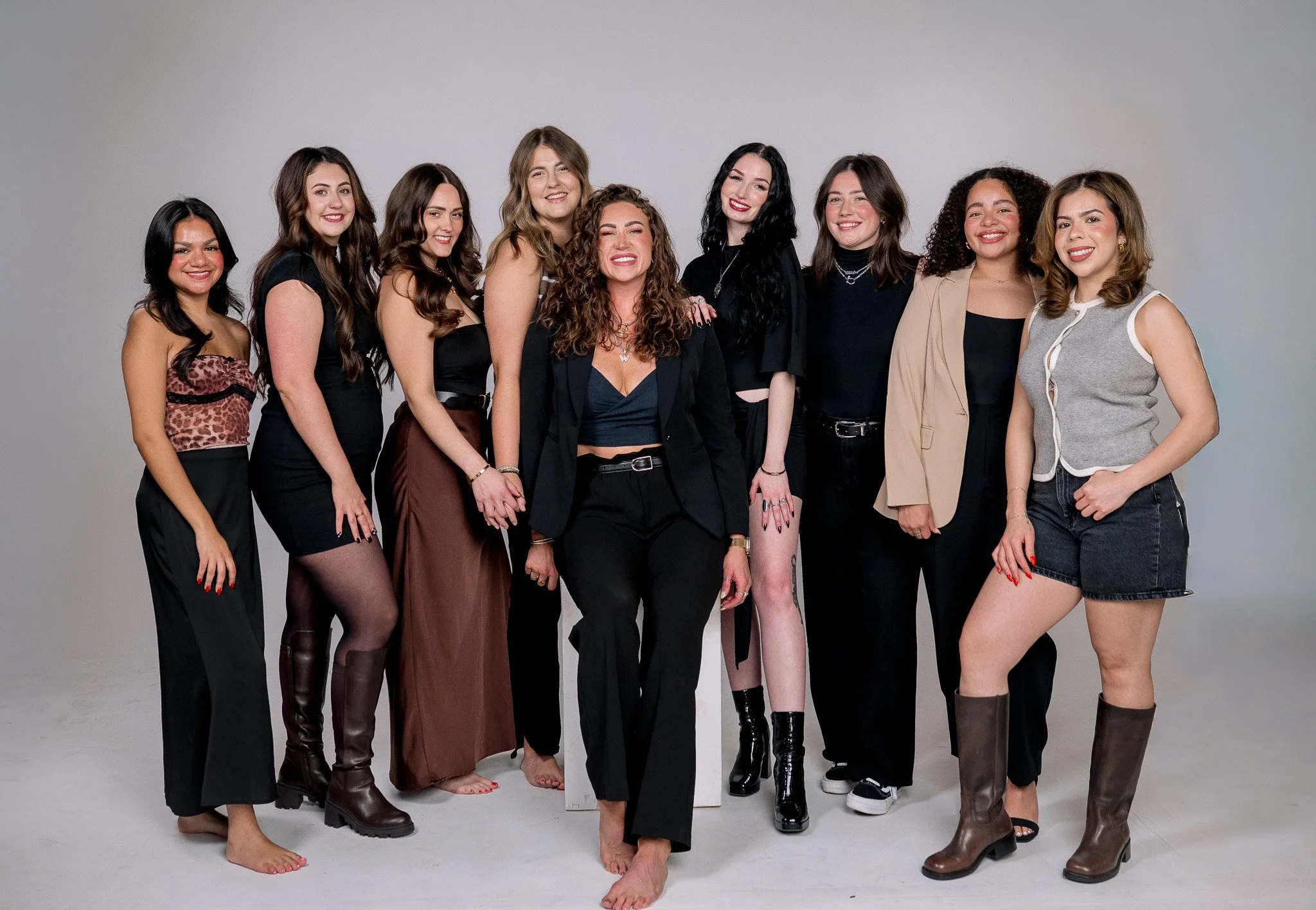 Group of 10 women standing together in a photo studio, smiling, dressed in a mix of casual and stylish outfits.