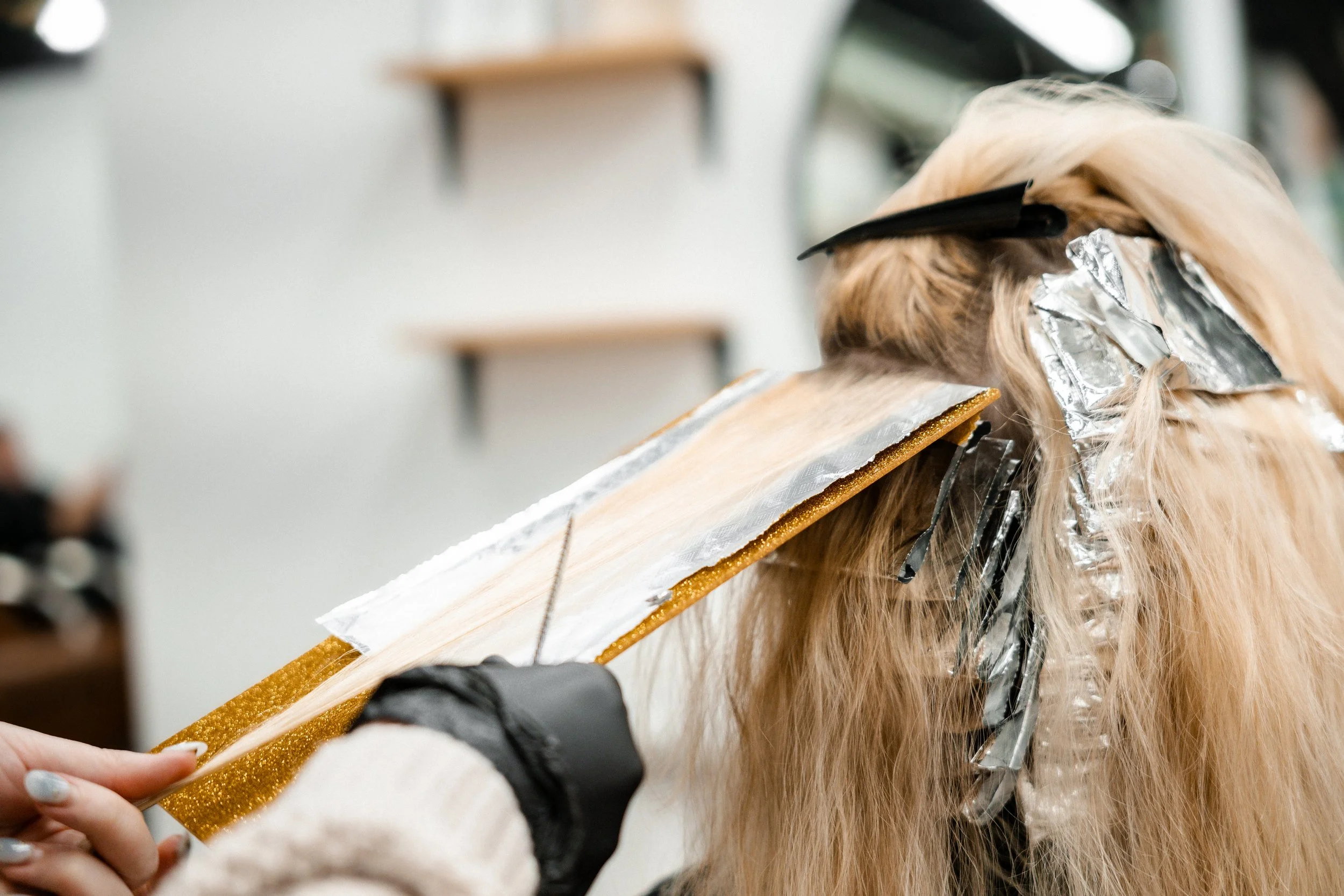 Person getting hair dyed with aluminum foil strips in a salon.
