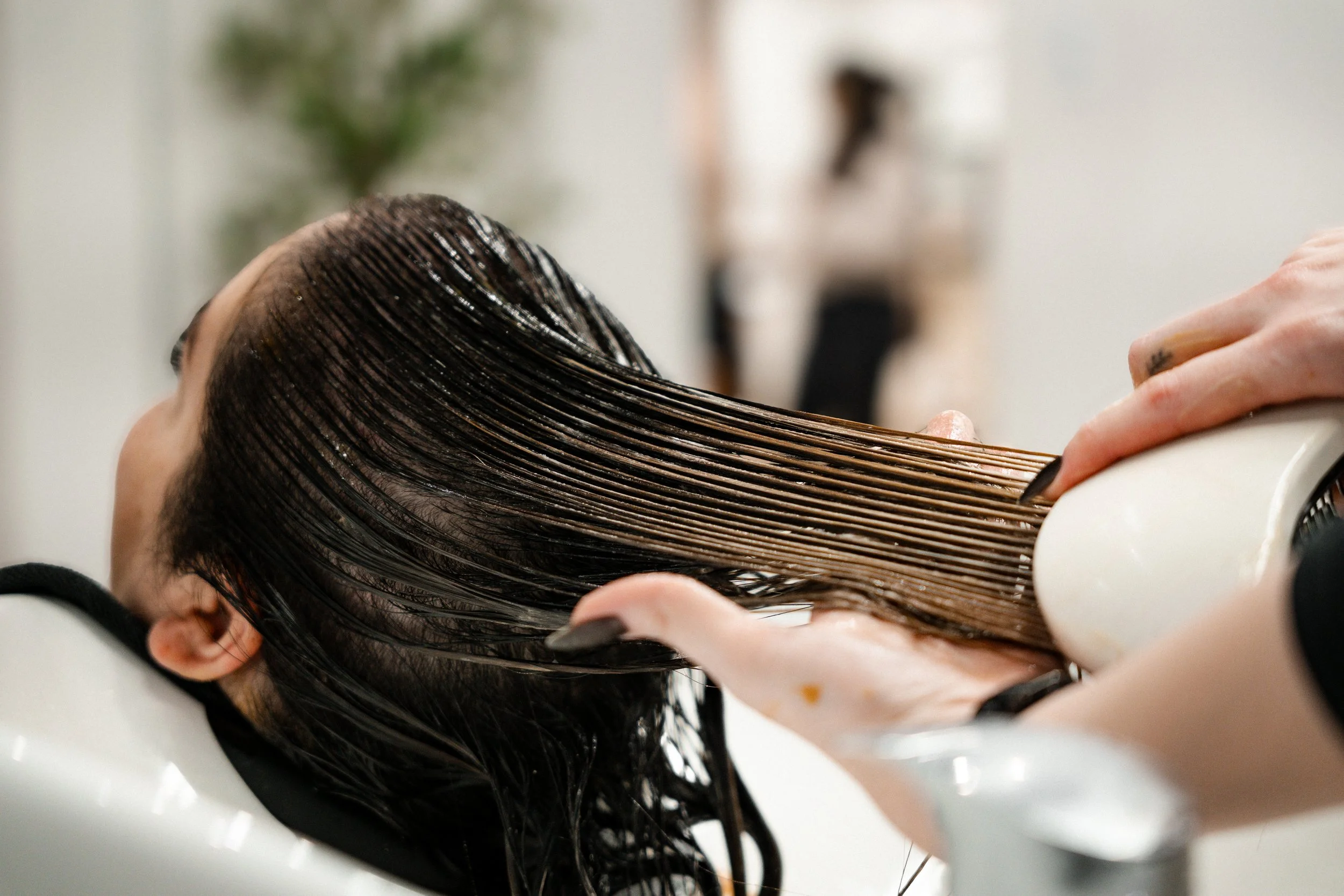 A person getting their hair washed at a salon, with hair wet and combed back, leaning back with head resting in a sink.