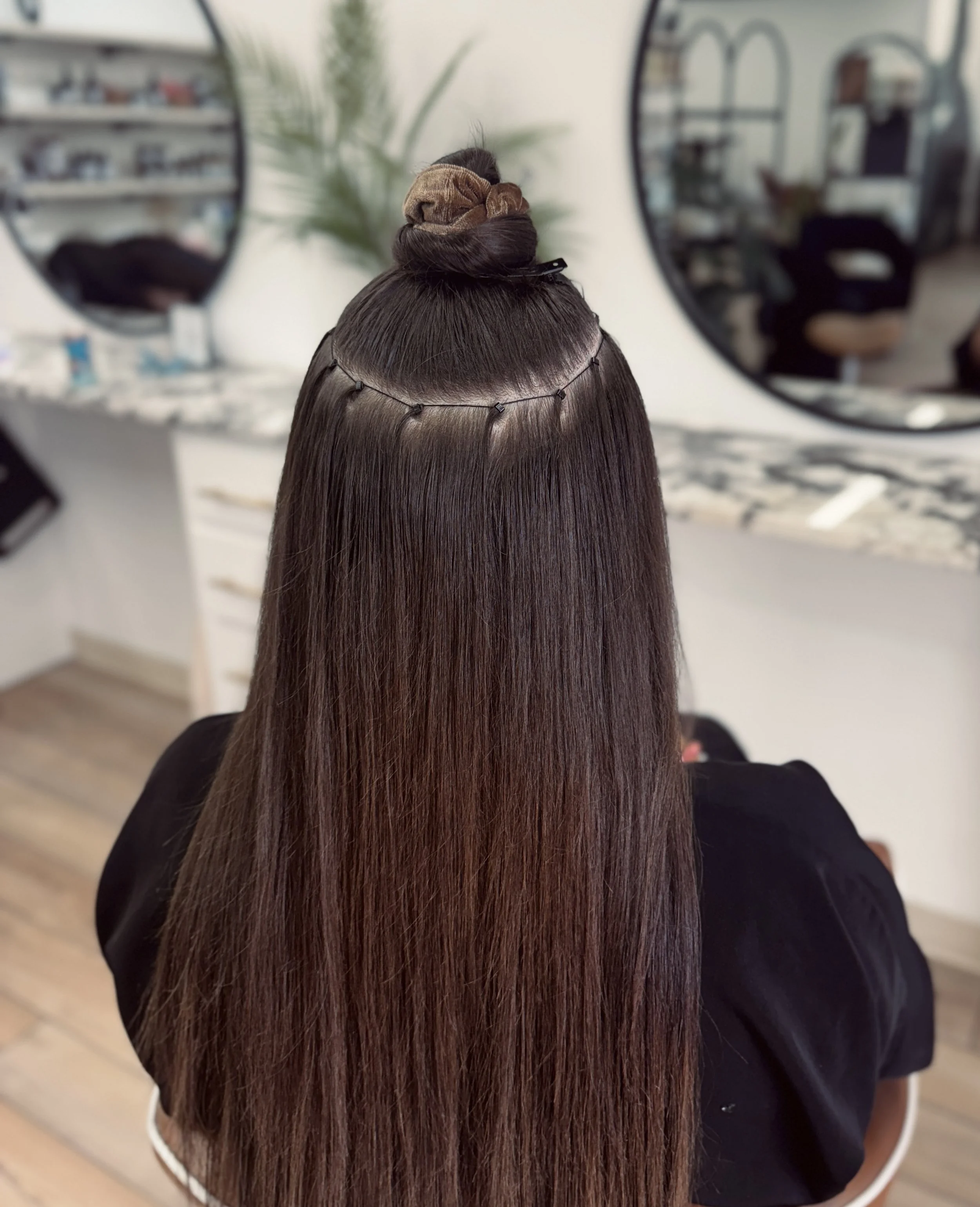 Woman with straight, long brown hair at a hair salon, with her hair sectioned and pulled up in a bun on top of her head, secured with hair clips and a small hair wrap.