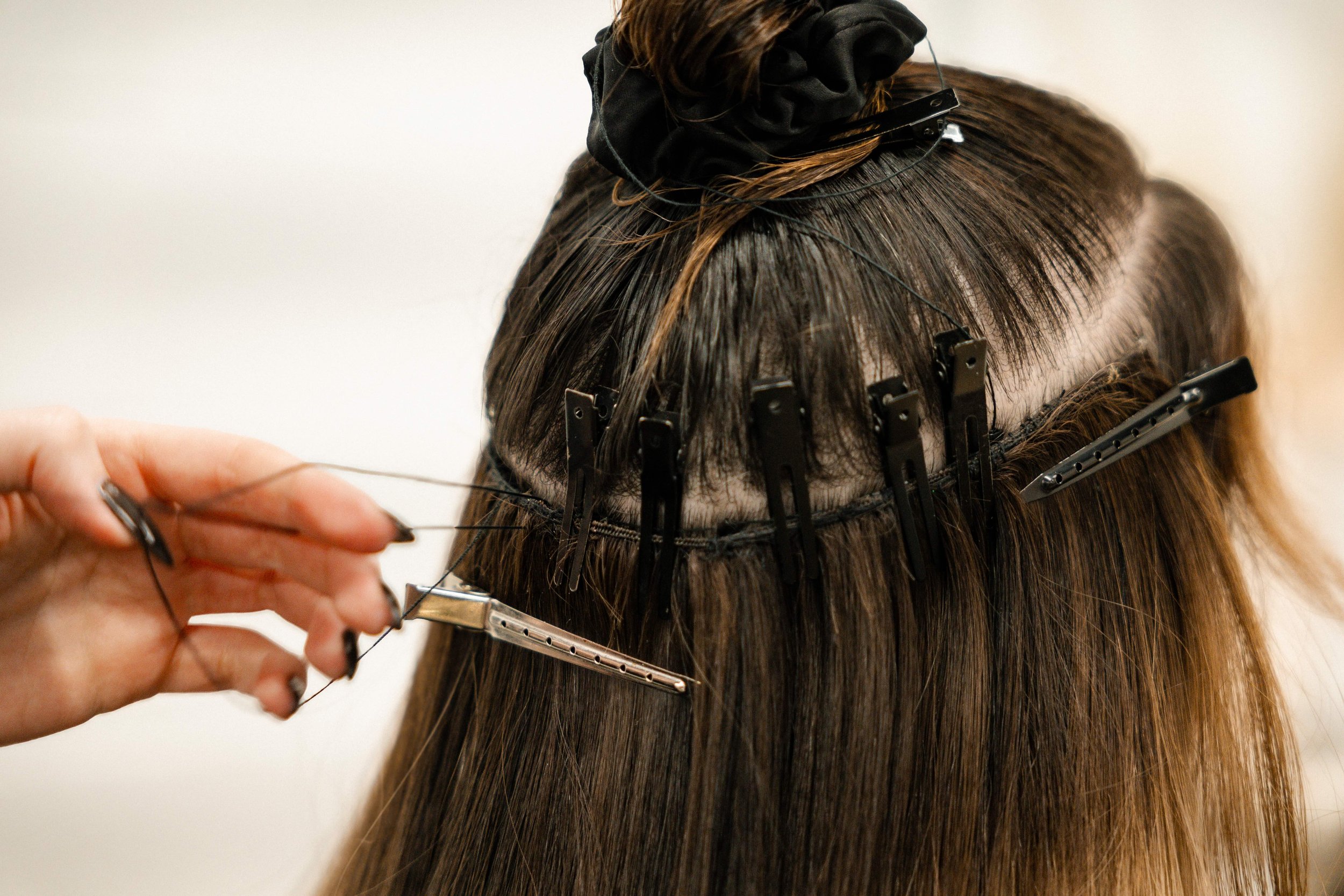 Hair stylist uses a weaving needle to sew hair extensions onto a person's head, with hair clips holding the hair and extension in place.