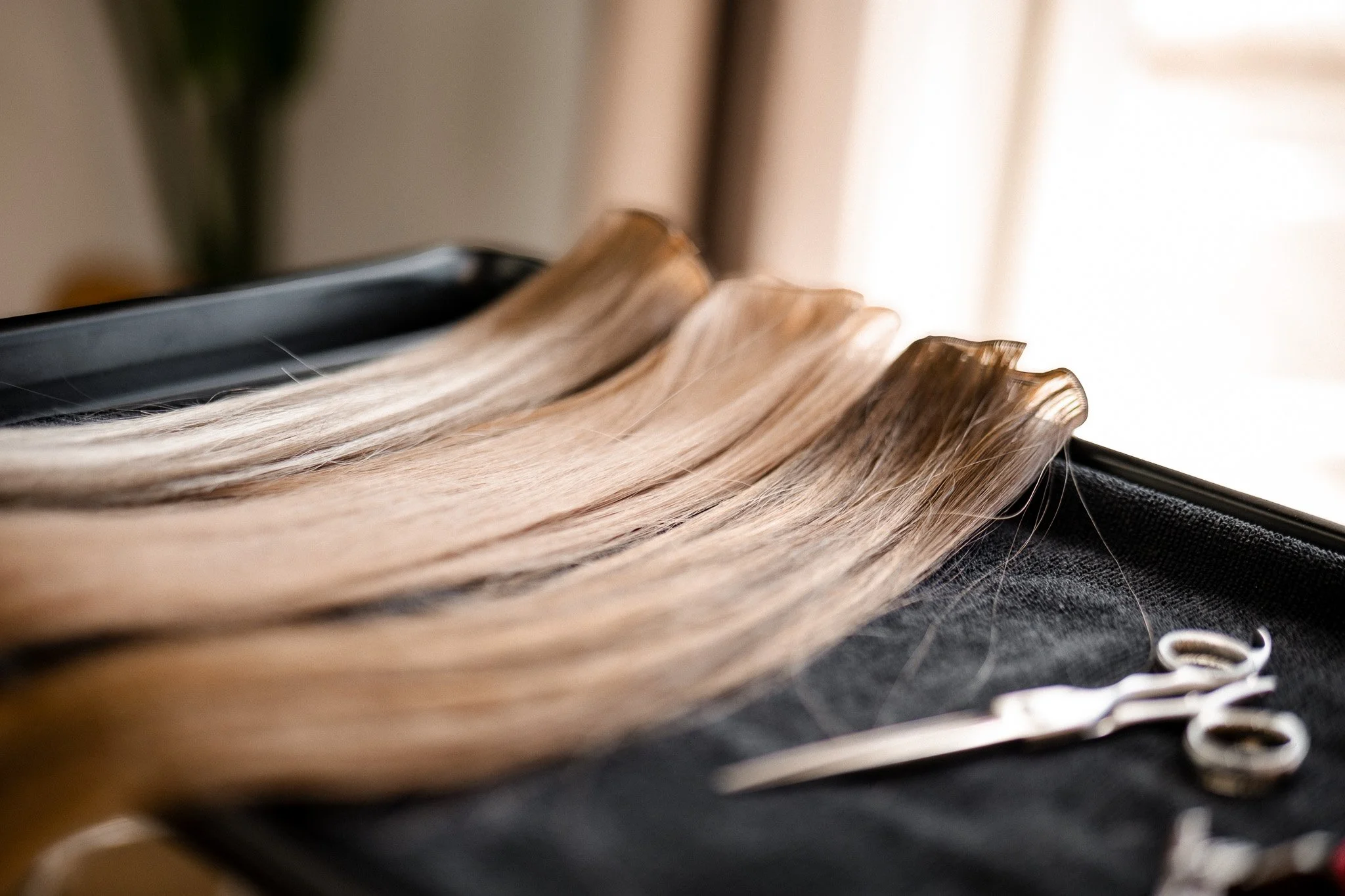 A close-up of blonde hair on a black flat iron hair straightener.