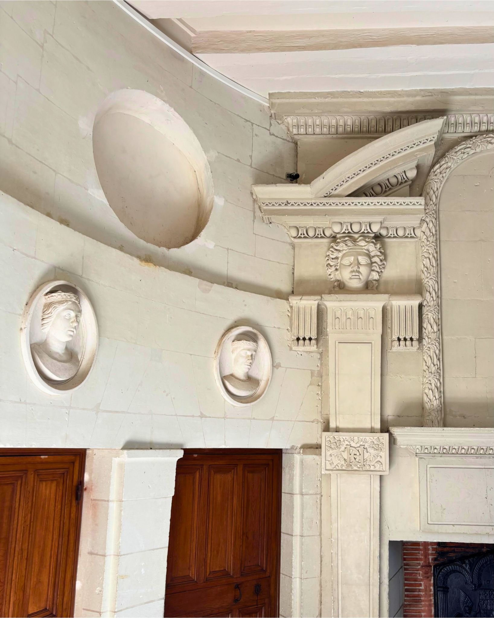 Décor architectural en pierre blanche avec des bustes et un visage sculpté, éléments de décoration classiques autour d'une cheminée.