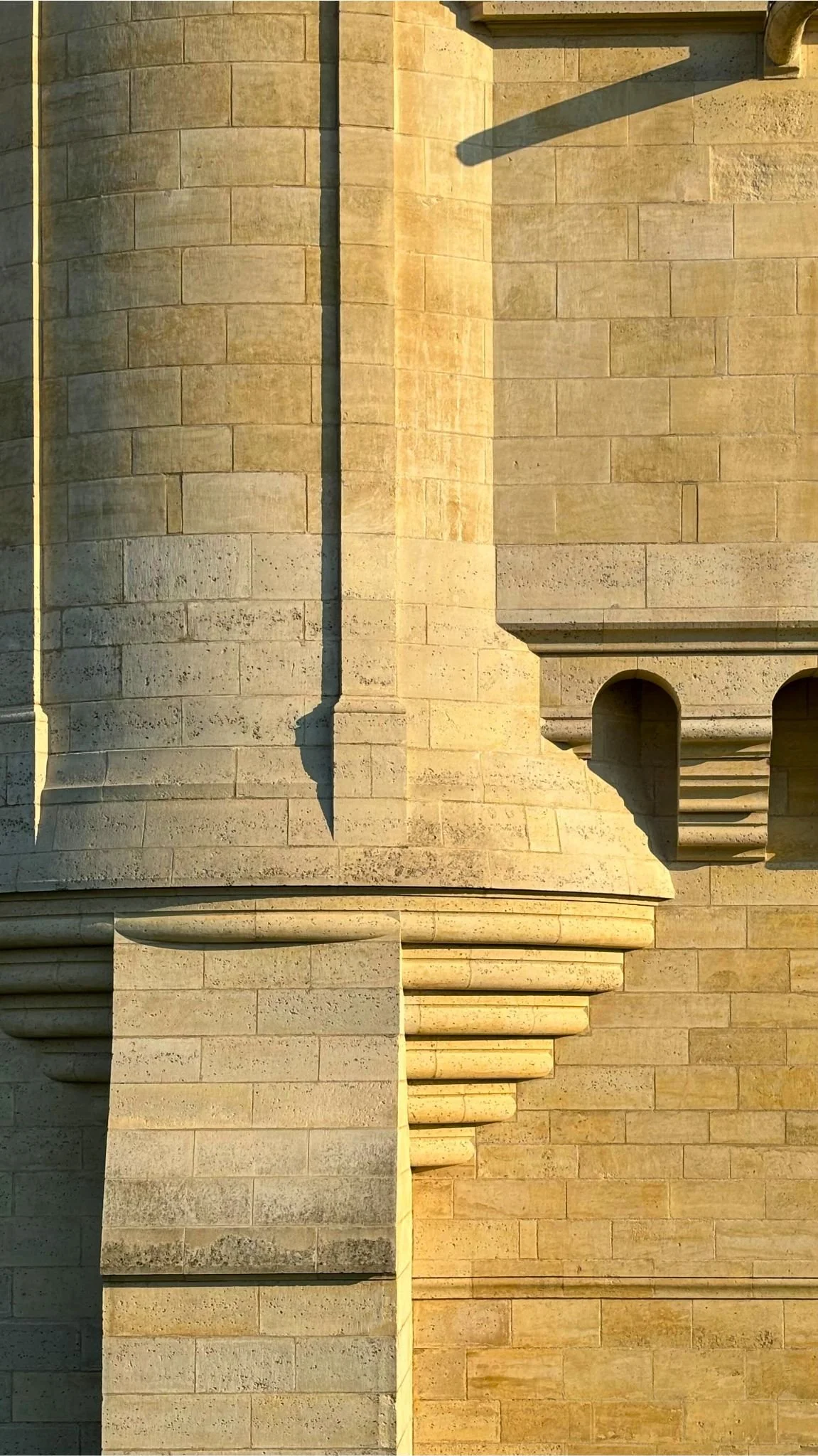 Murs en pierre beige d'un bâtiment ancien, avec des détails architecturaux tels que des moulures et des colonnes, éclairés par la lumière du soleil.