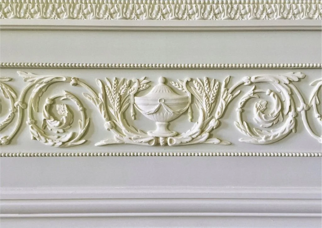 Pose et assemblage d'ornements en stuc : urne, rinceaux et perles s'assemblent dans une harmonie de gris nacrés