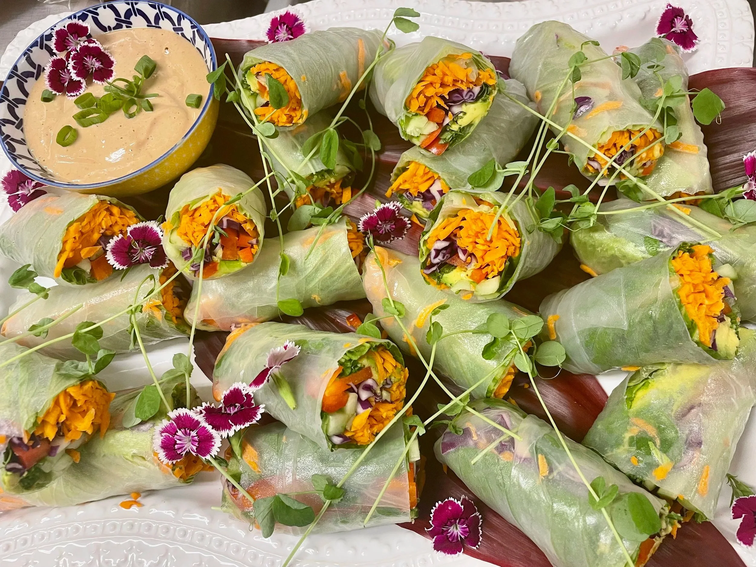 Fresh vegetable spring rolls with edible flowers and microgreens on a decorative tray.