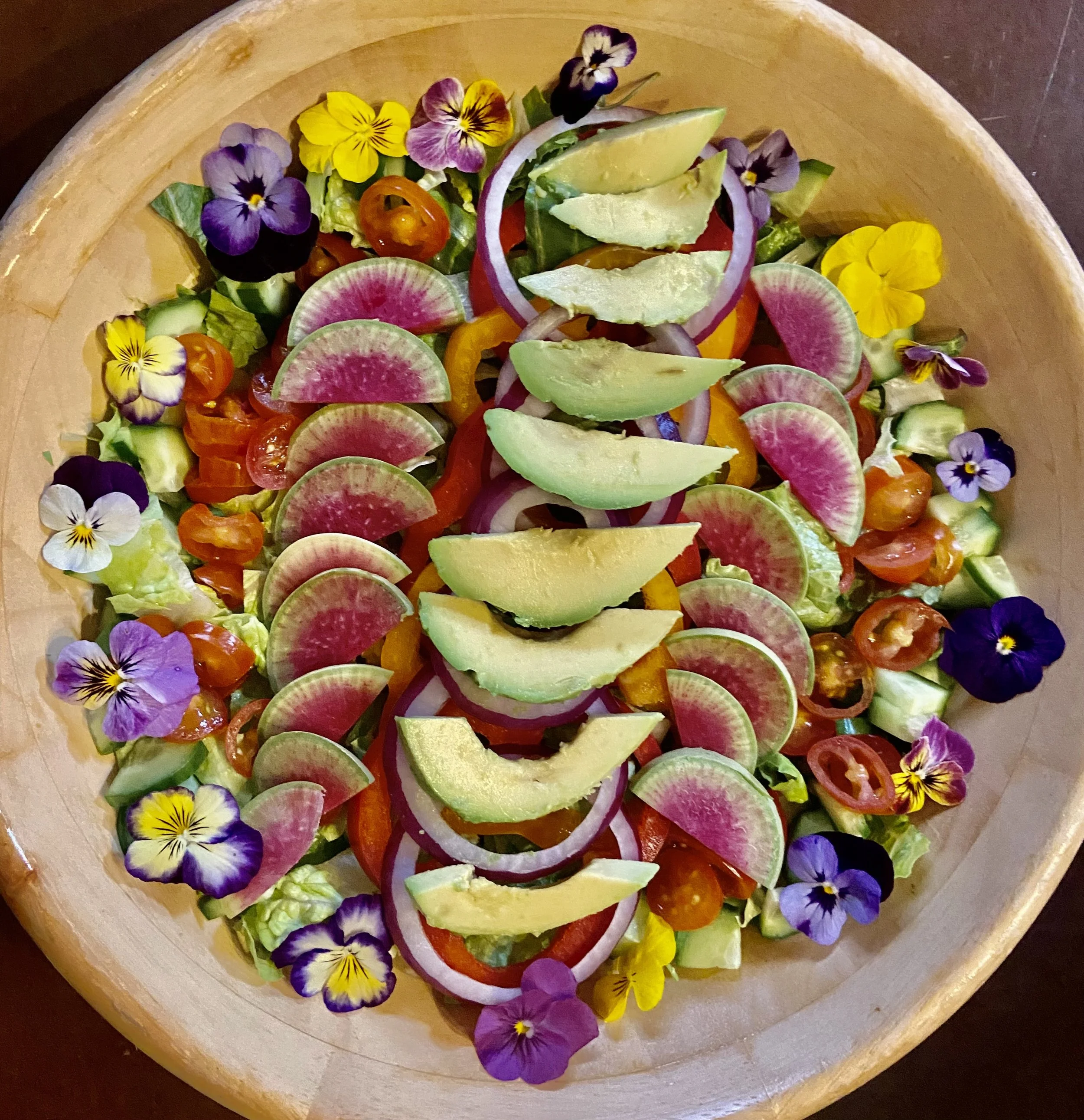 Colorful salad with radishes, cherry tomatoes, avocado and edible flowers in a wooden bowl.