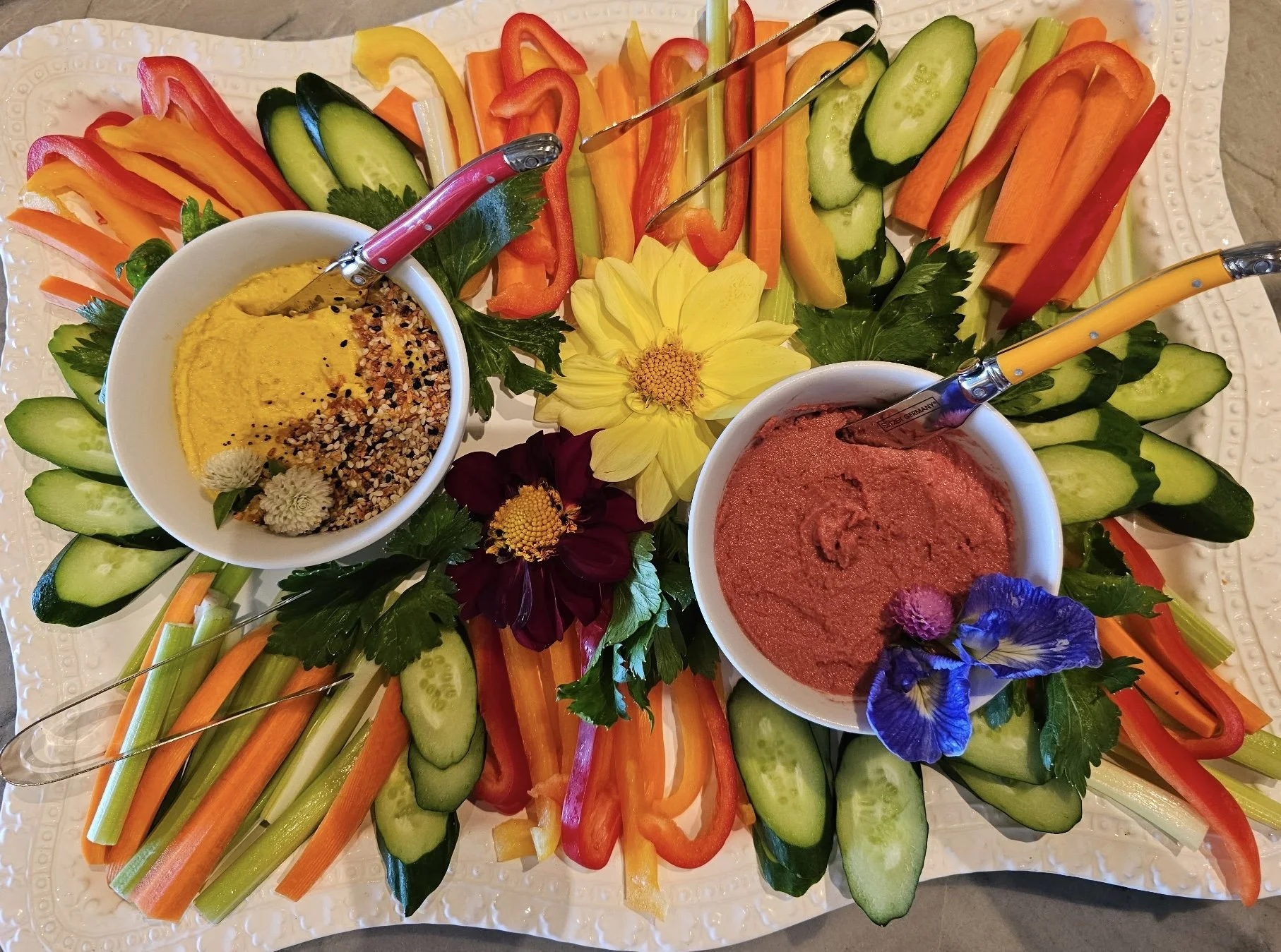 Fresh vegetables arranged around hummus and beet dip with edible flowers and herbs