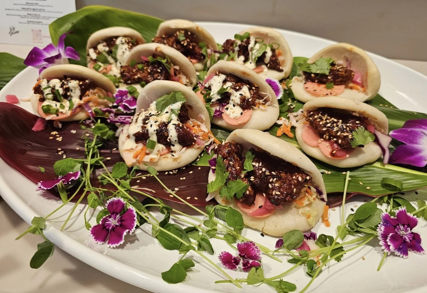 Asian bao buns with meat, vegetables, sesame seeds, herbs and purple flowers
