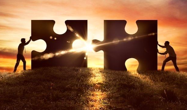 Two people pushing apart large puzzle pieces at sunset, with the sun shining through the gaps.