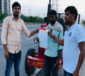 Three young men standing on the side of a highway with a homemade vehicle, holding a paper and contact information, under cloudy skies with power lines in the background.