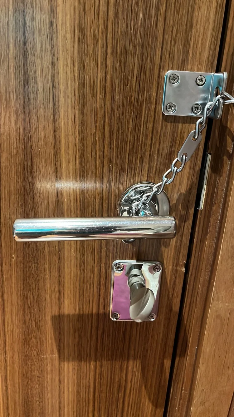 A wooden door with a metal latch and chain lock, a silver door handle, and a locking mechanism.