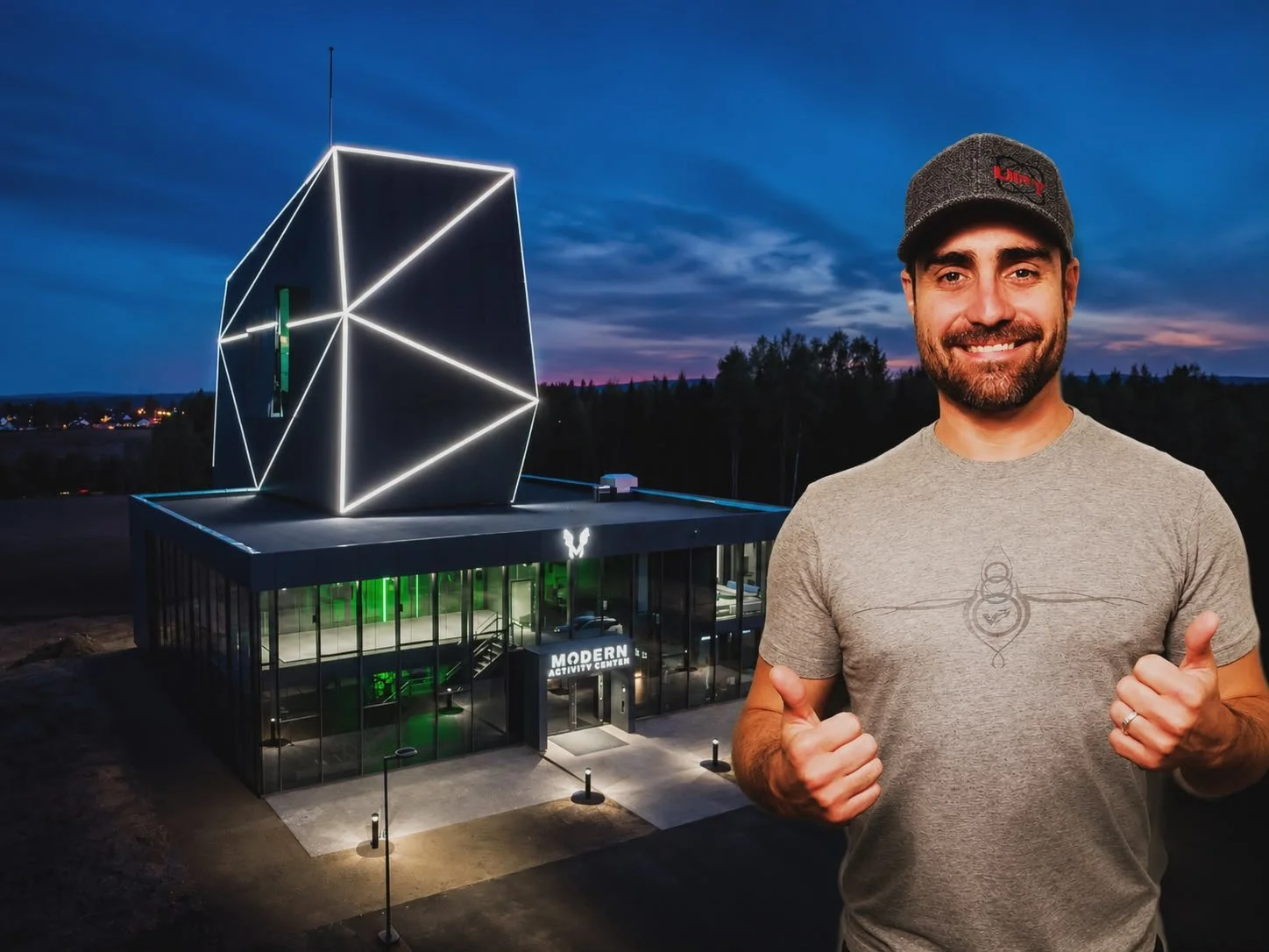 A smiling man with a beard wearing a gray cap and t-shirt giving thumbs up in front of a modern activity center building with the sign 'MODERN ACTIVITY CENTER' and illuminated geometric art installation on rooftop during evening.