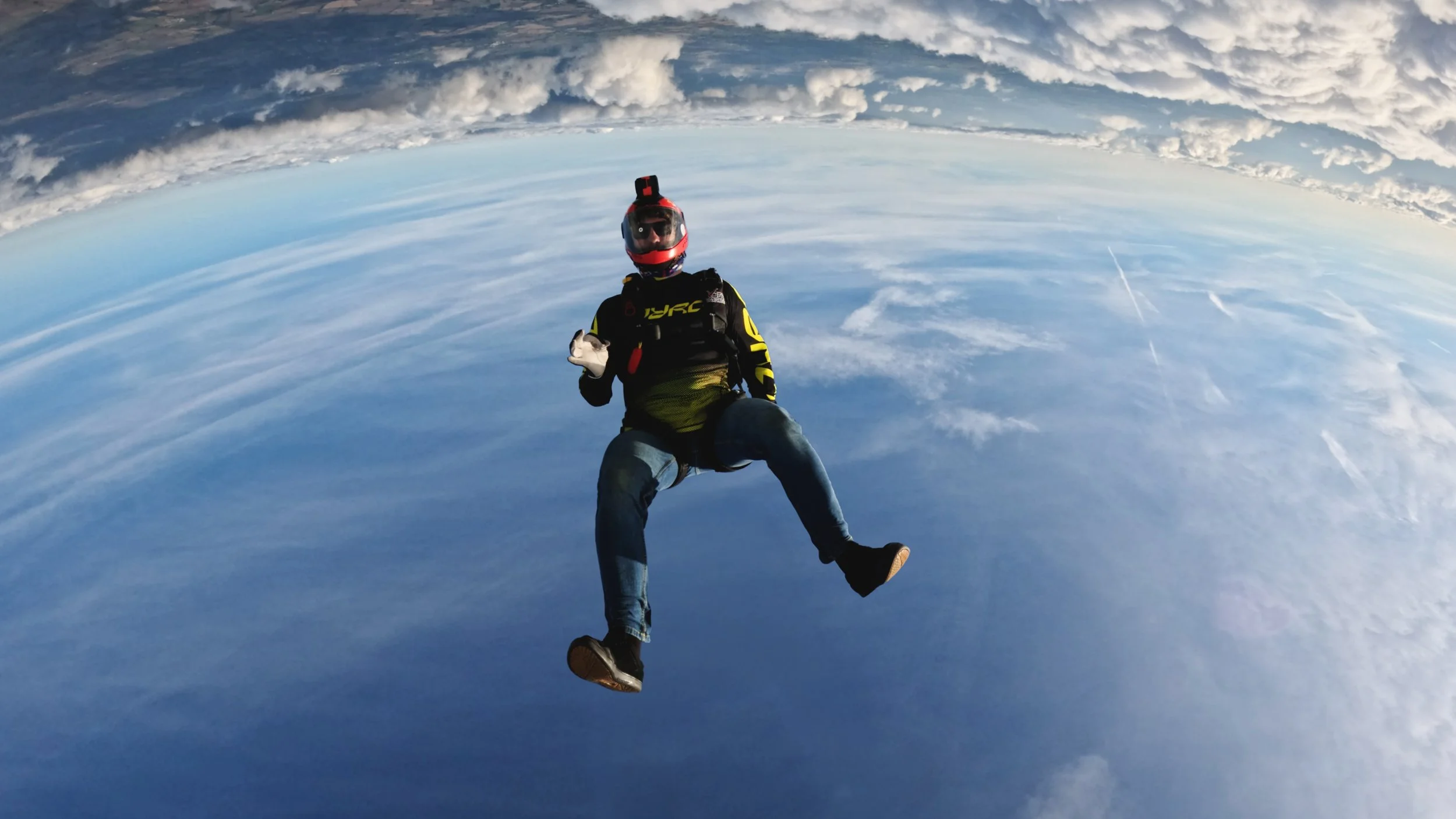 Person in a helmet and black jacket floating above the clouds during the daytime.