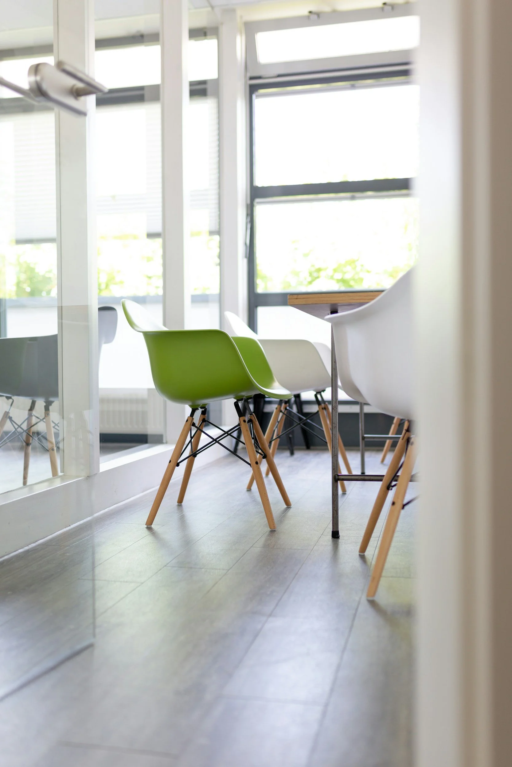 Modern meeting room with green and white chairs around a table, bright natural light from large windows.