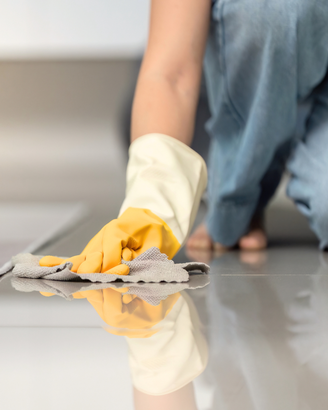 Person cleaning a gray tile floor with a gray cloth, wearing yellow rubber gloves.