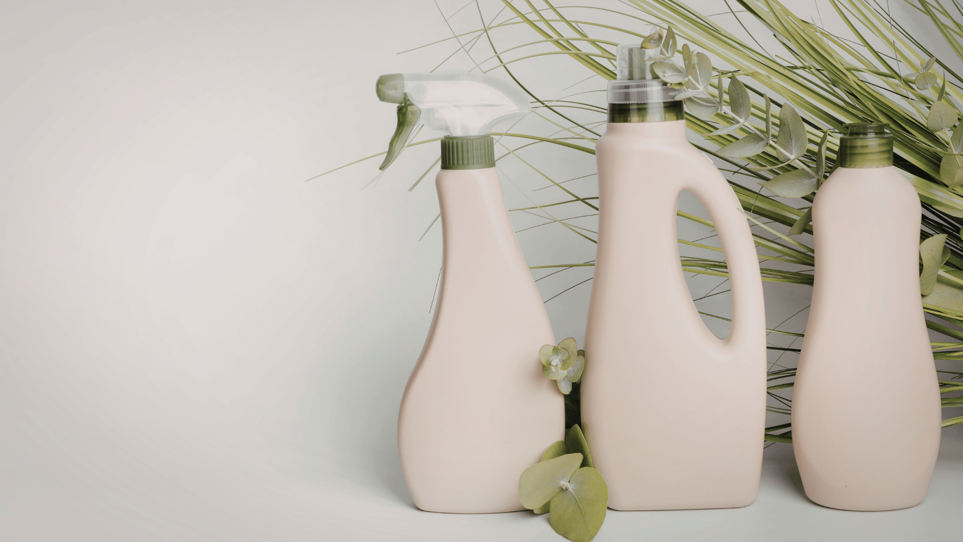 Three beige plastic bottles with green caps, one spray, one with a handle, and one without; arranged in front of green leaves and foliage.