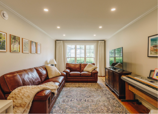 Living room with leather sofas, a patterned area rug, a TV on a wooden stand, and framed artwork on light-colored walls.