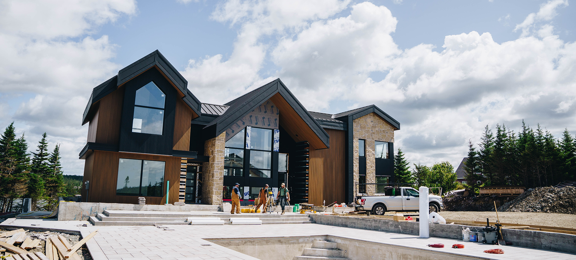 Modern house under construction with workers and construction materials in the front yard, blue sky with clouds