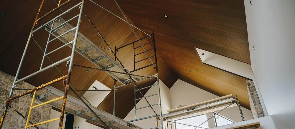 Interior of a building under construction or renovation, with scaffolding set up and a sloped wooden ceiling.