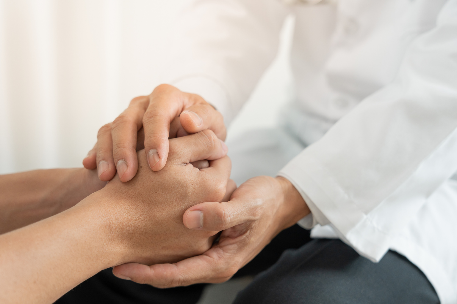 Two people holding hands, one with darker skin and the other with lighter skin, in a comforting or supportive gesture.