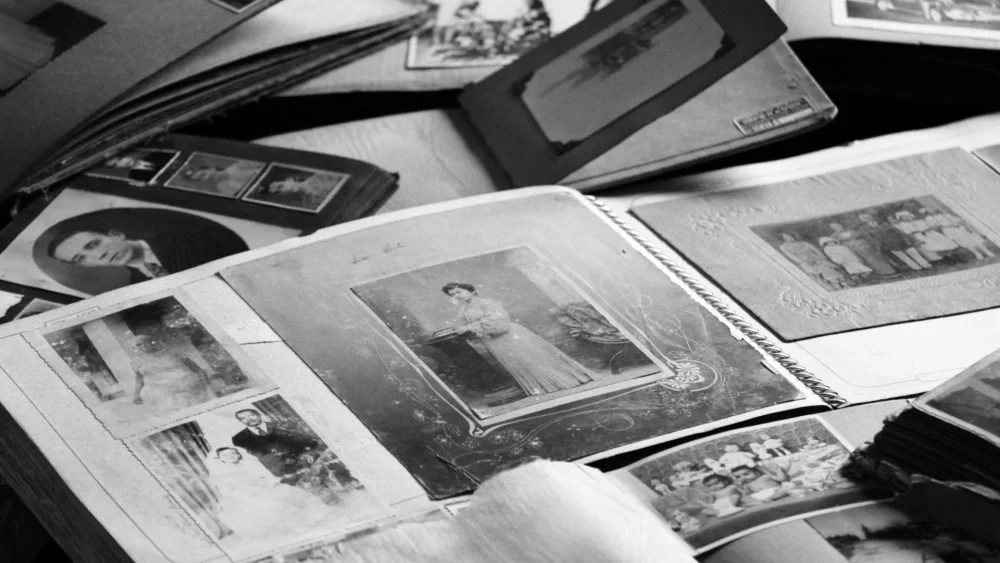 Open photograph albums displaying black and white vintage photographs of people and landscapes.