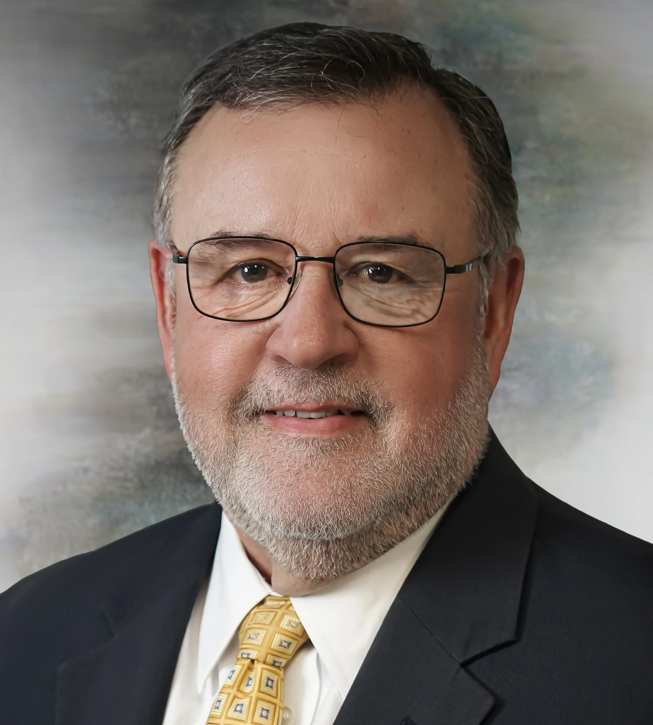A middle-aged man with glasses wearing a dark pinstripe suit, white shirt, and a brown patterned tie, posing for a professional headshot against a dark blue background.