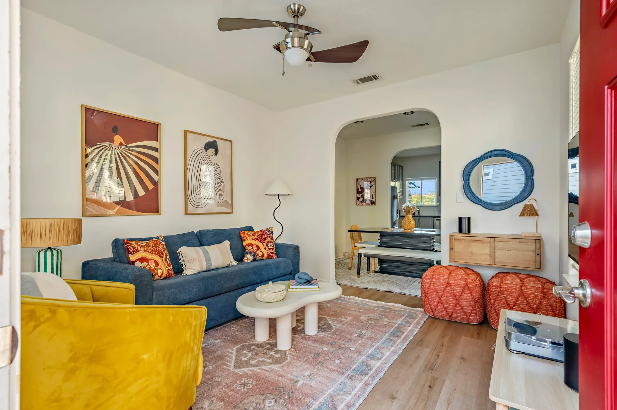 Short-term rental living room design with navy sofa, mustard accent chair, colorful figure art, and arched doorway to dining room — Austin TX.