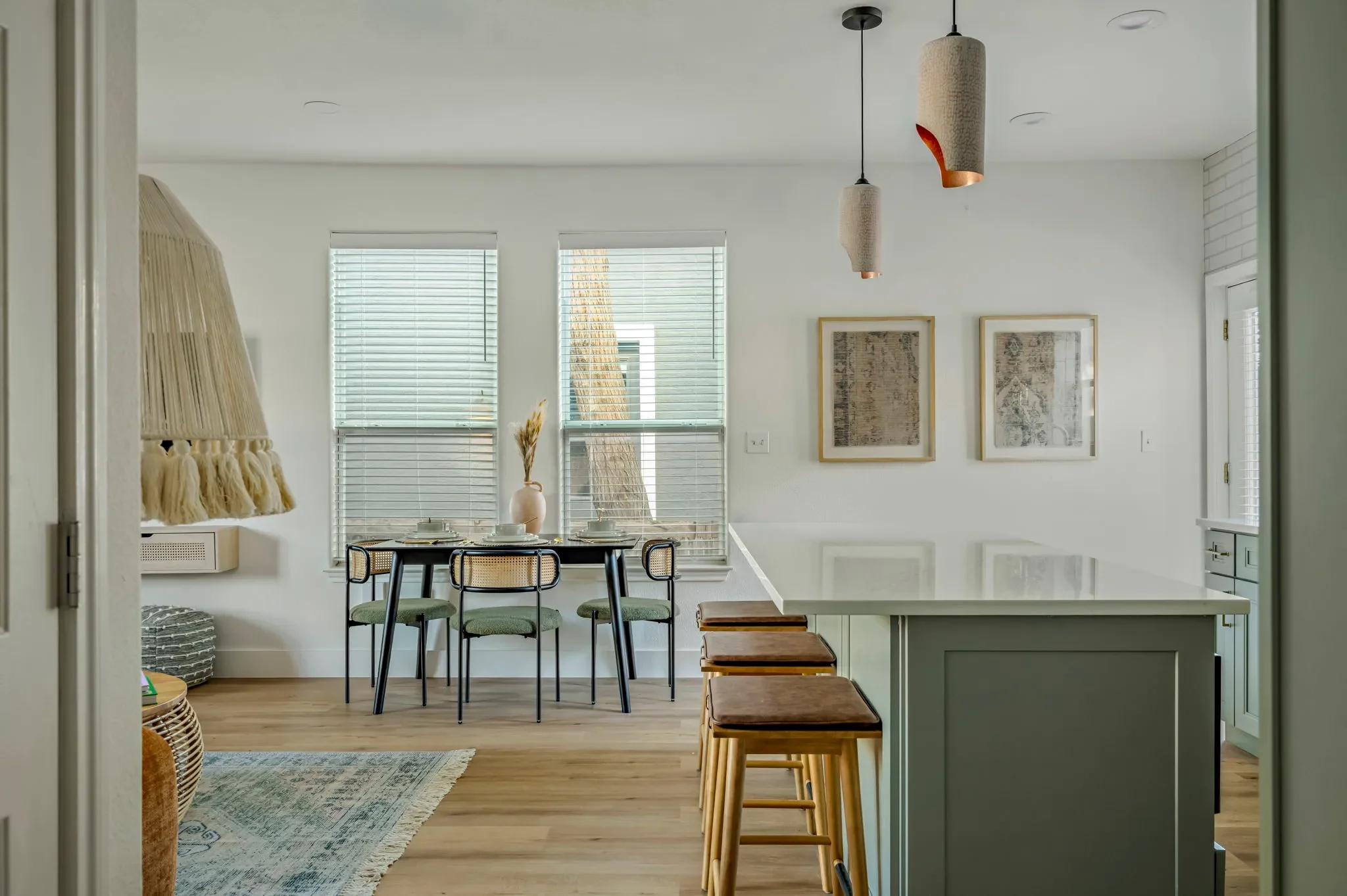 Short-term rental open plan design with sage green kitchen island, fringe pendant lights, and view to dining room — Austin TX.