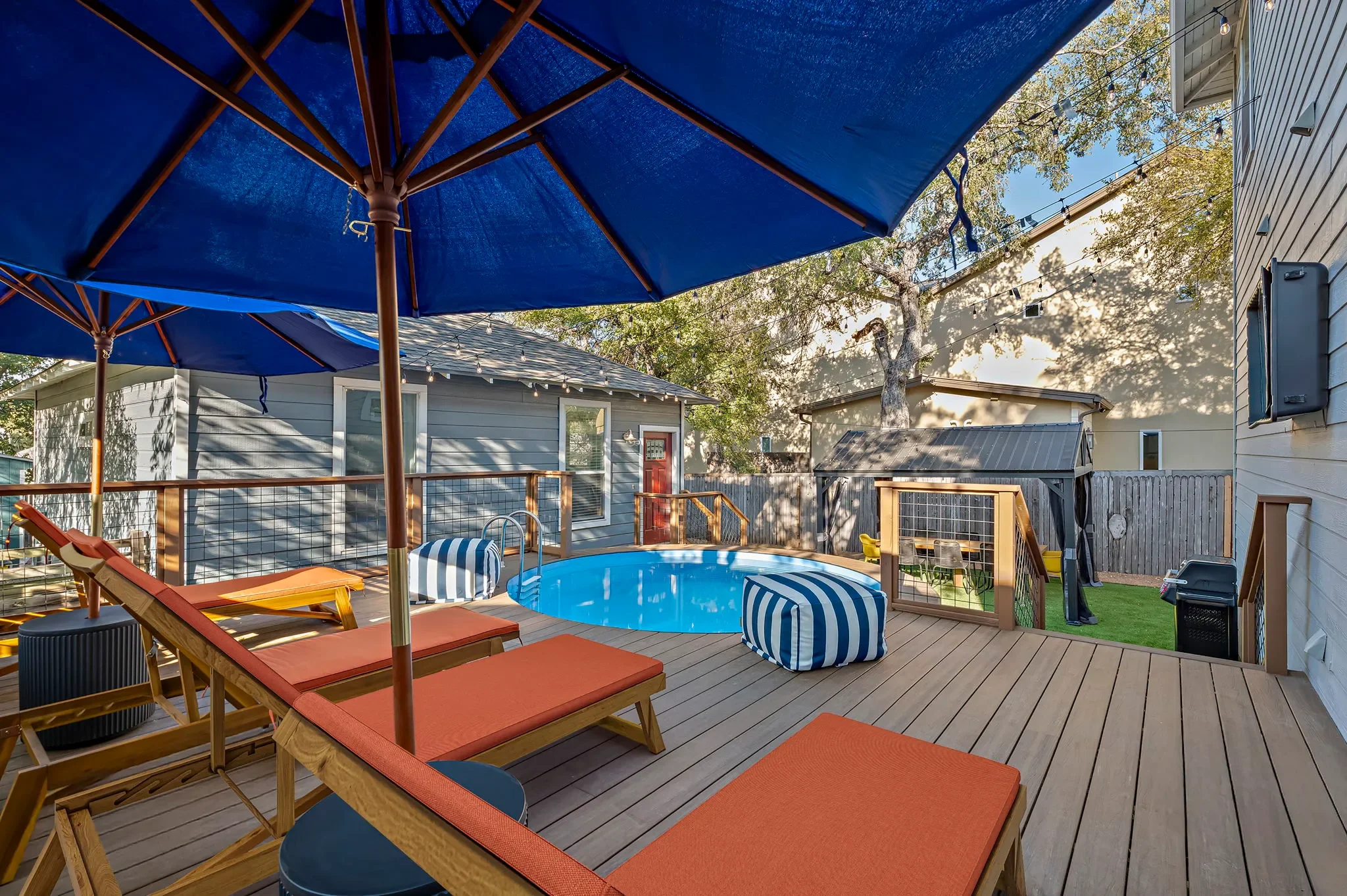 Short-term rental backyard design with round plunge pool, orange lounge chairs, blue umbrella, and wood deck — Austin TX.