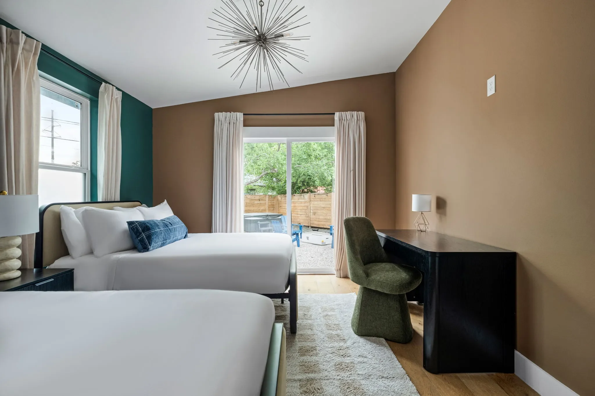 Short-term rental double bedroom design with tan and teal walls, two queen beds, black desk, and sputnik chandelier — Austin TX.