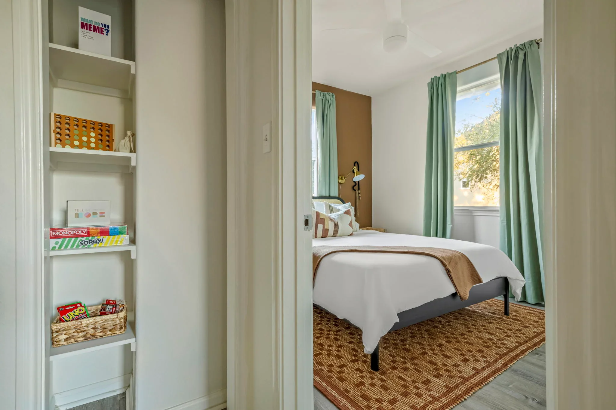 Airbnb interior design detail with built-in shelving stocked with board games, and view into brown accent wall bedroom — Austin TX.