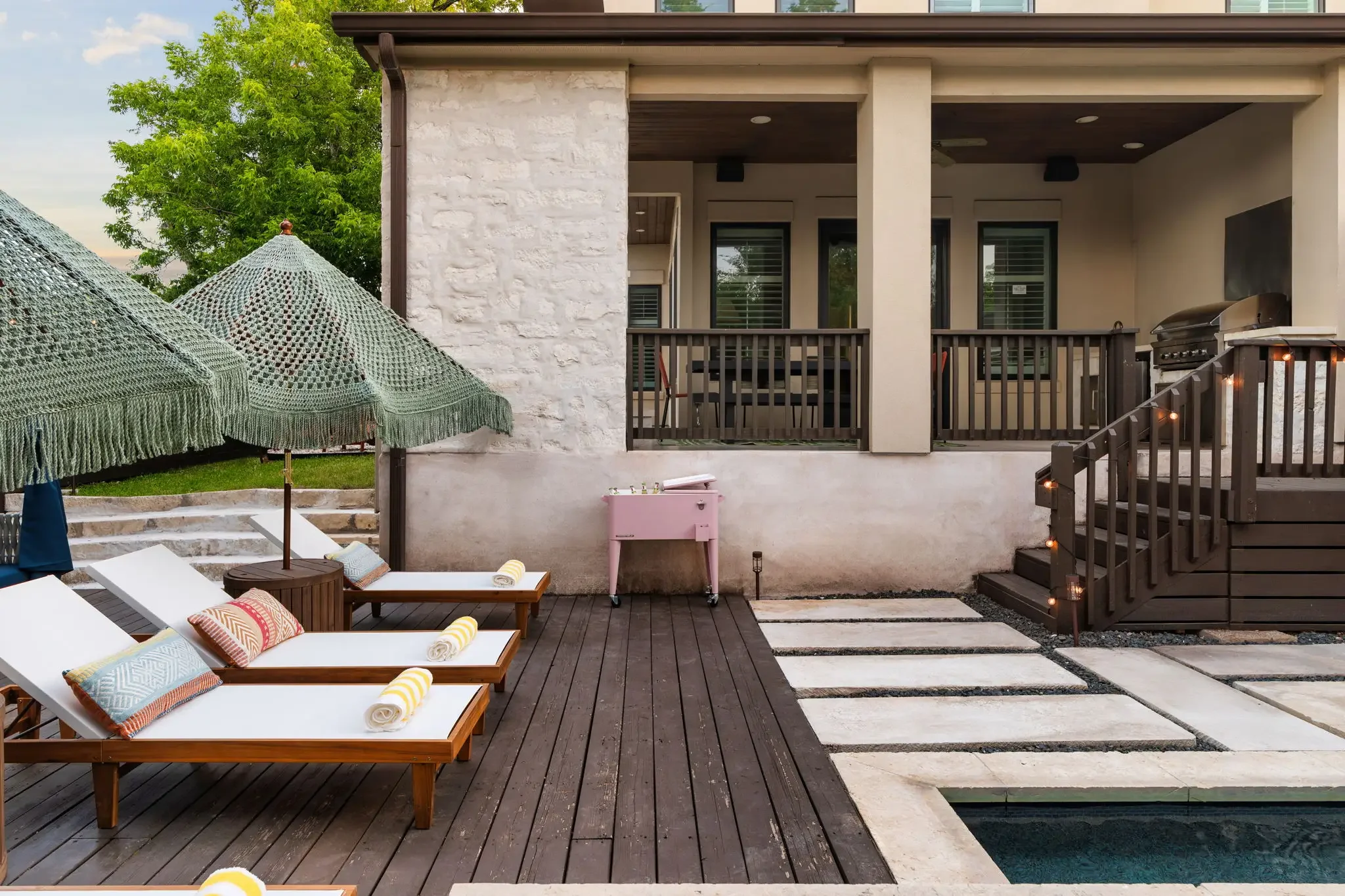 Short-term rental backyard design with wood lounge chairs, macrame umbrellas, and deck leading to outdoor entertaining area — Austin TX.