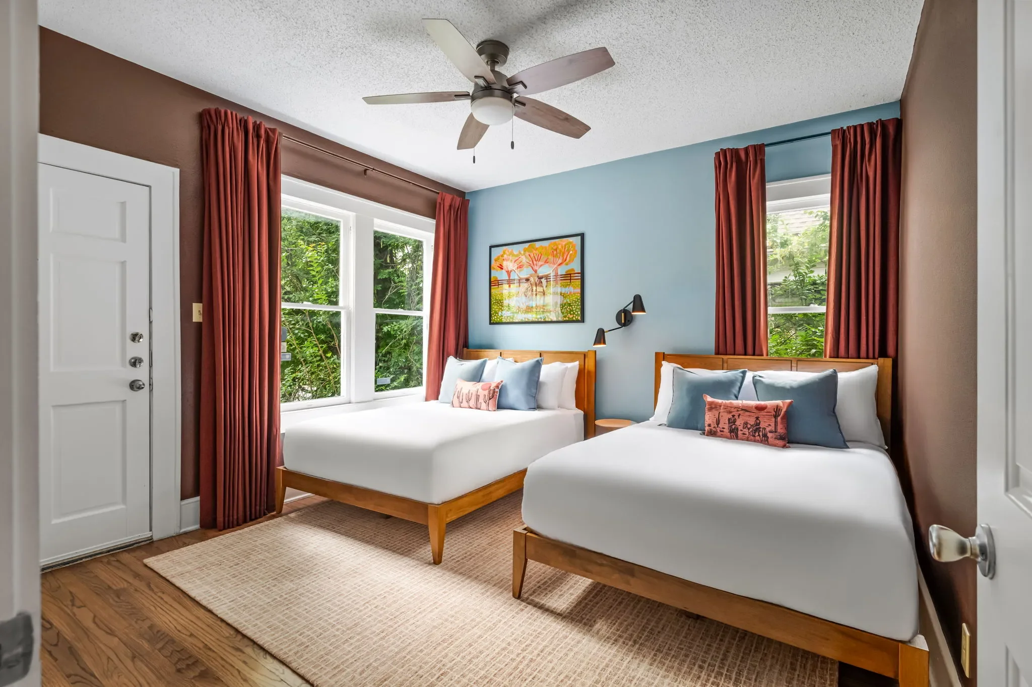 Airbnb double bedroom design with blue and brown walls, two wood bed frames, rust curtains, and longhorn artwork — Austin TX.