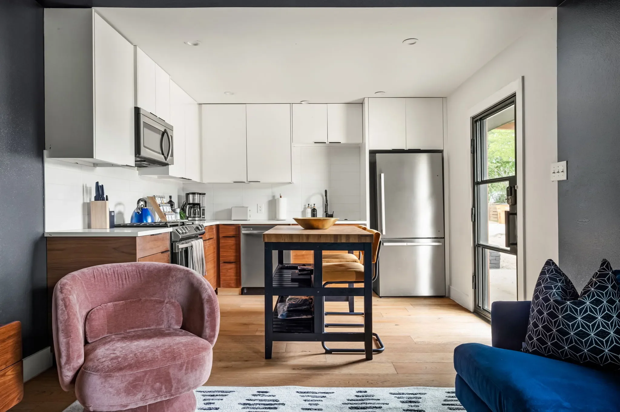 Short-term rental guest house kitchen design with white cabinets, wood lower cabinets, stainless appliances, and butcher block island — Austin TX.