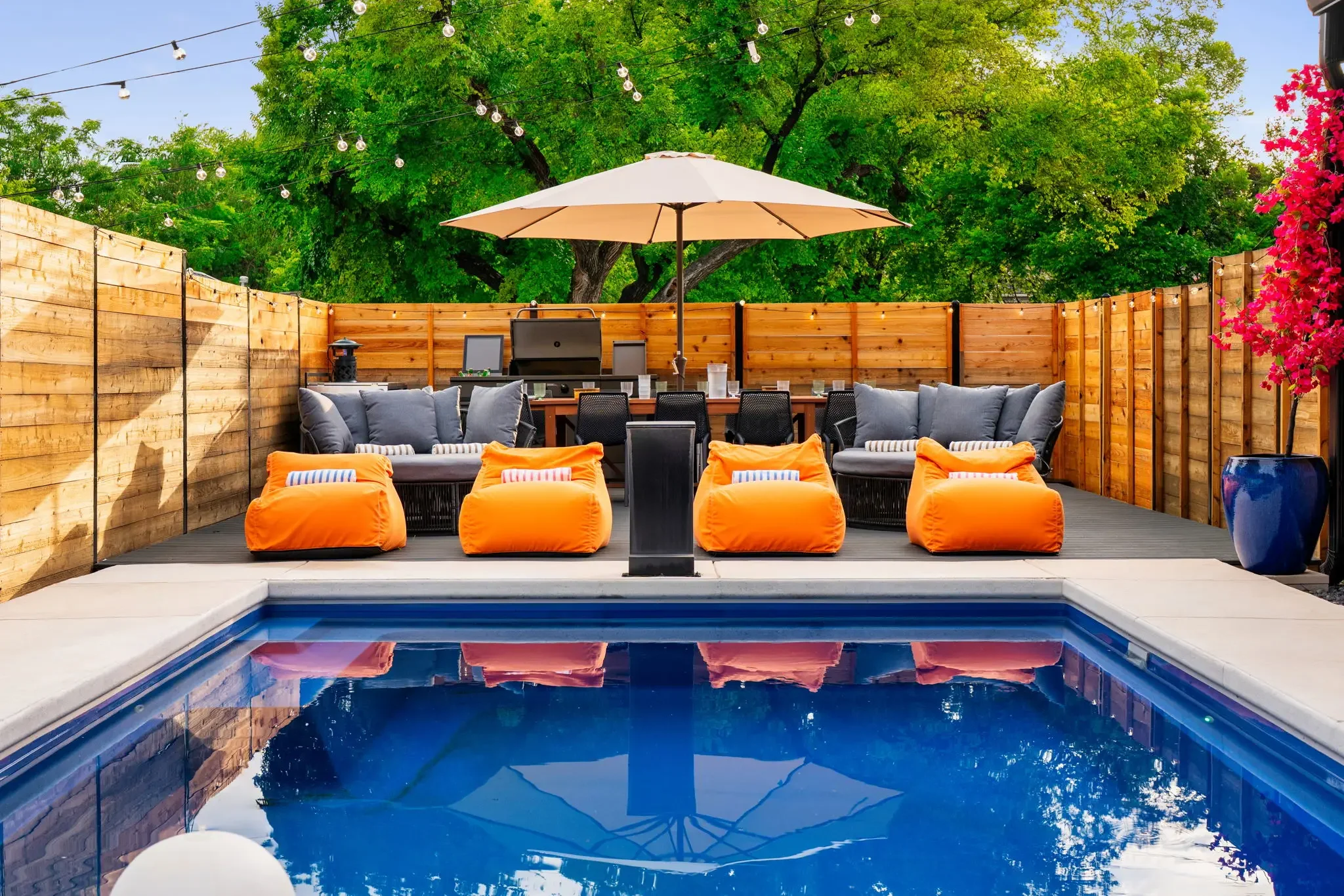 Airbnb pool design with orange bean bag loungers, outdoor dining table, grill station, and string lights — Austin TX.