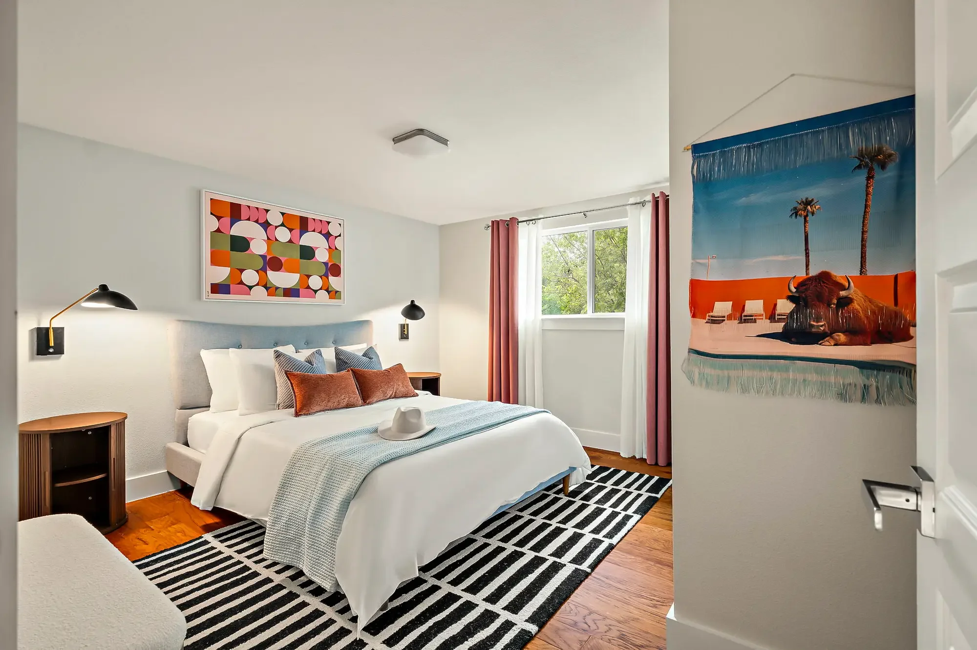 Airbnb bedroom design with teal upholstered headboard, retro circle art, black stripe rug, pink curtains, and California pool photography — Austin TX.