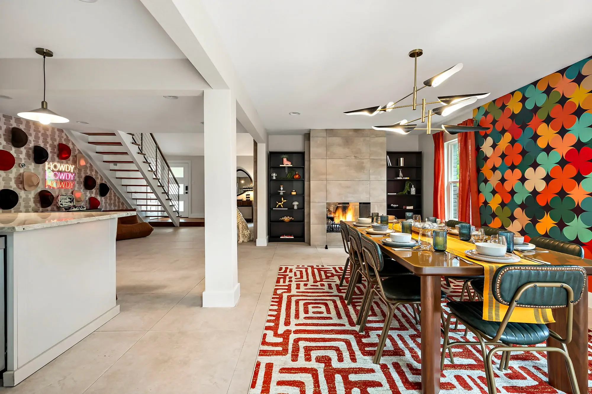 Short-term rental dining room design with retro floral mural, long dining table, red geometric rug, and floating staircase — Austin TX.