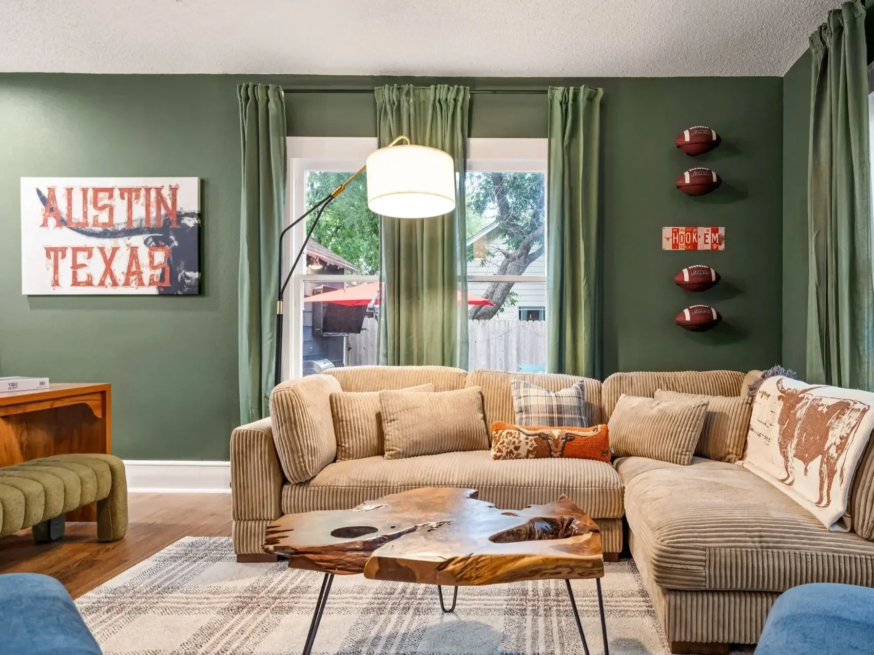 Modern living room in an Austin short-term rental featuring an orange sectional sofa, a travertine coffee table, fur poufs, a black fireplace wall, and sliding glass doors opening to the backyard.