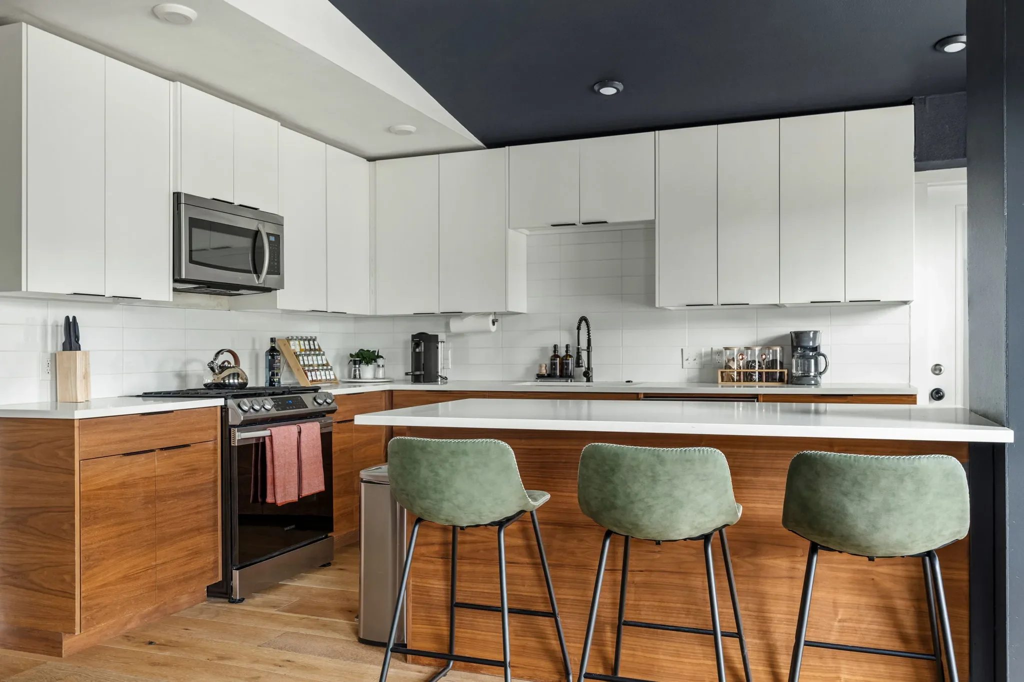 Airbnb kitchen design detail with white upper cabinets, wood lower cabinets, stainless appliances, and green bar stools — Austin TX.