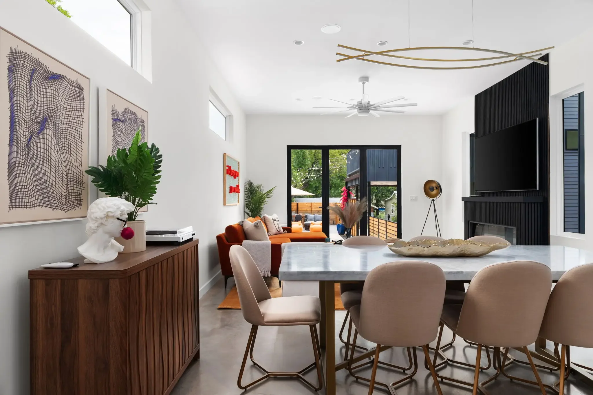 Short-term rental dining room design with marble table, velvet chairs, abstract wall art, greek bust decor, and view to living room and pool — Austin TX.