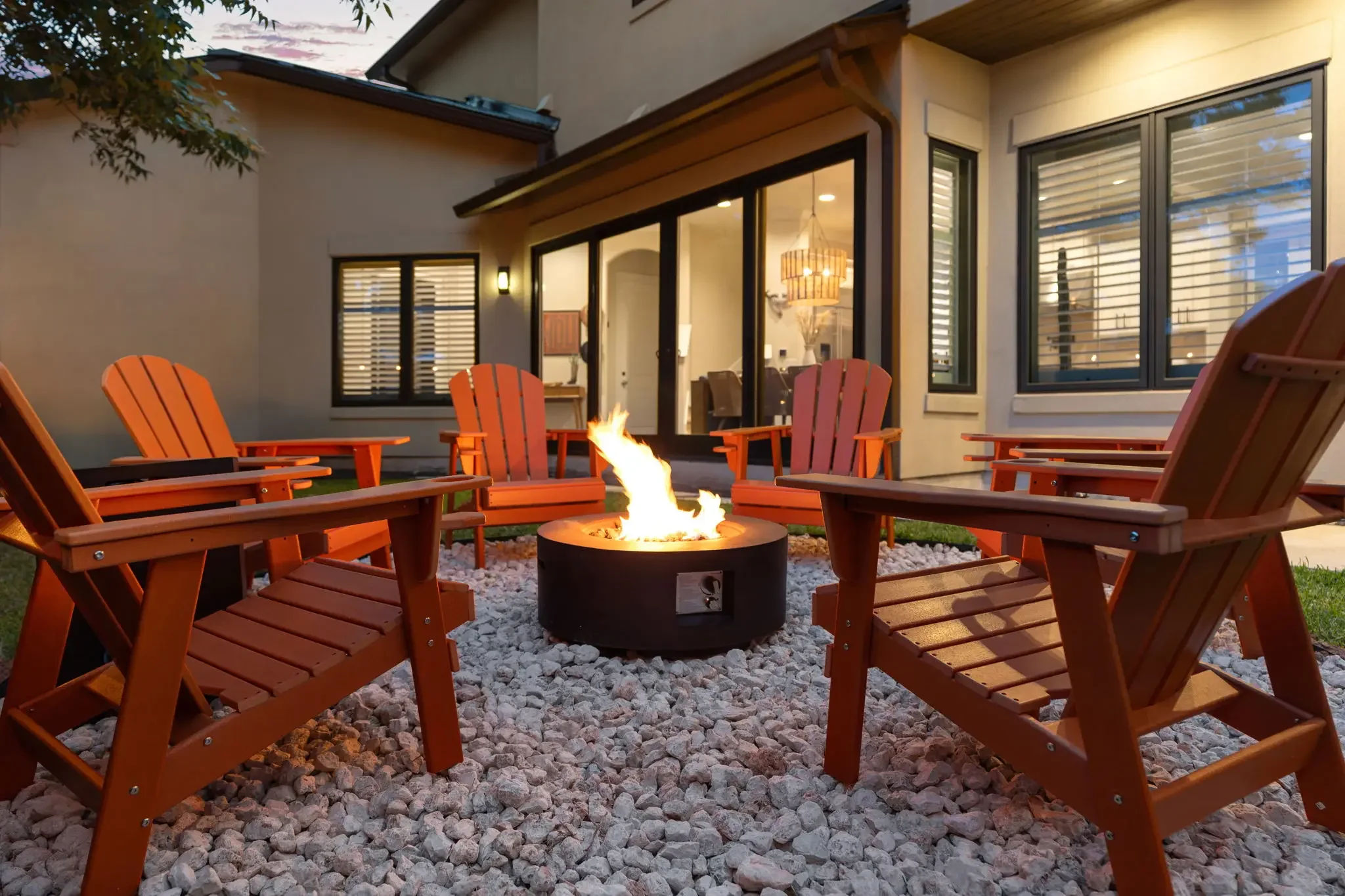 Airbnb outdoor design detail with lit fire pit surrounded by red Adirondack chairs on gravel patio — Austin TX.