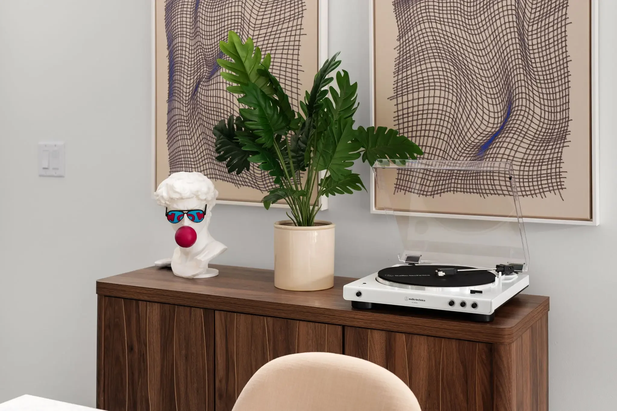 Airbnb interior design detail with wood sideboard, vinyl record player, greek bust with sunglasses, tropical plant, and abstract art — Austin TX.